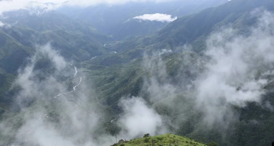 Clouds drifting through a deep green valley with a winding river below